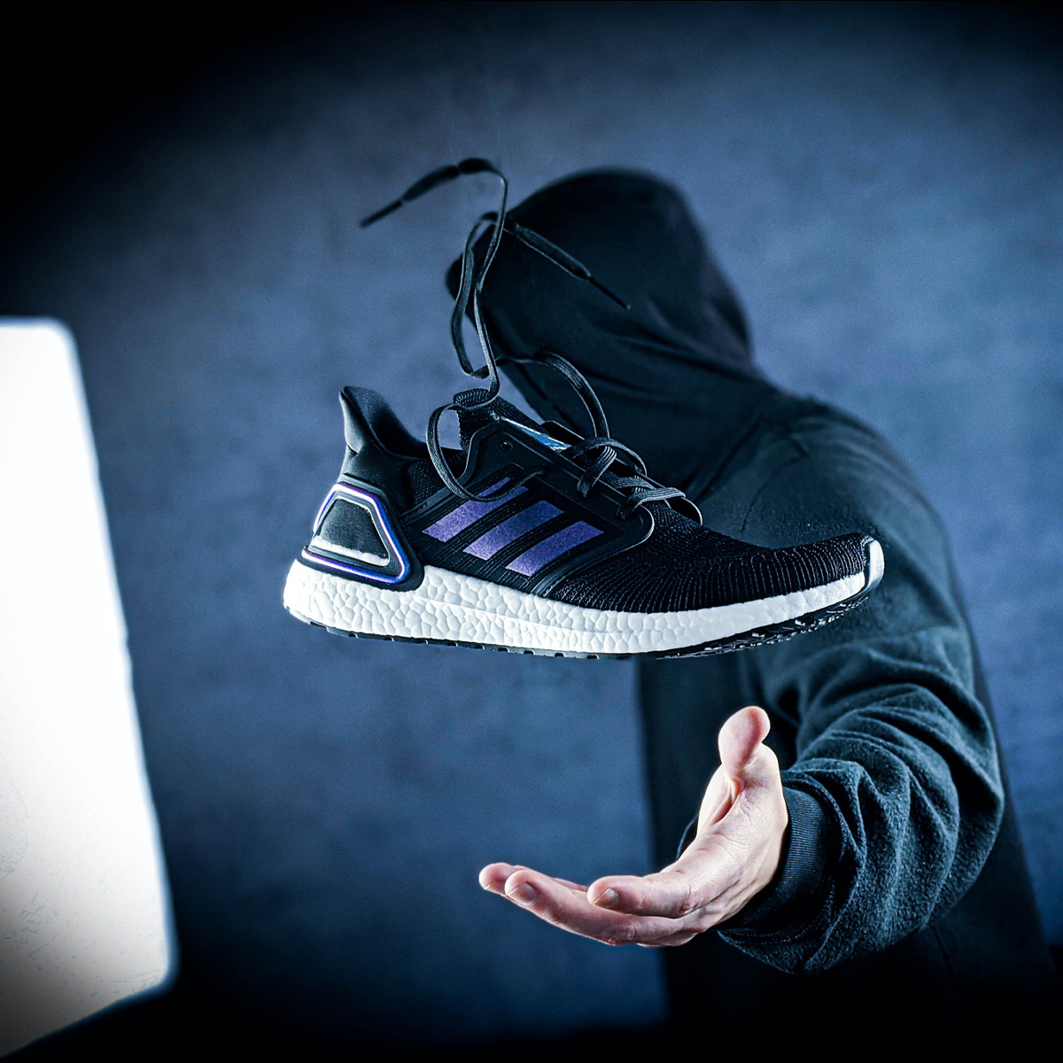 An Adidas shoe hovering above a man's hand